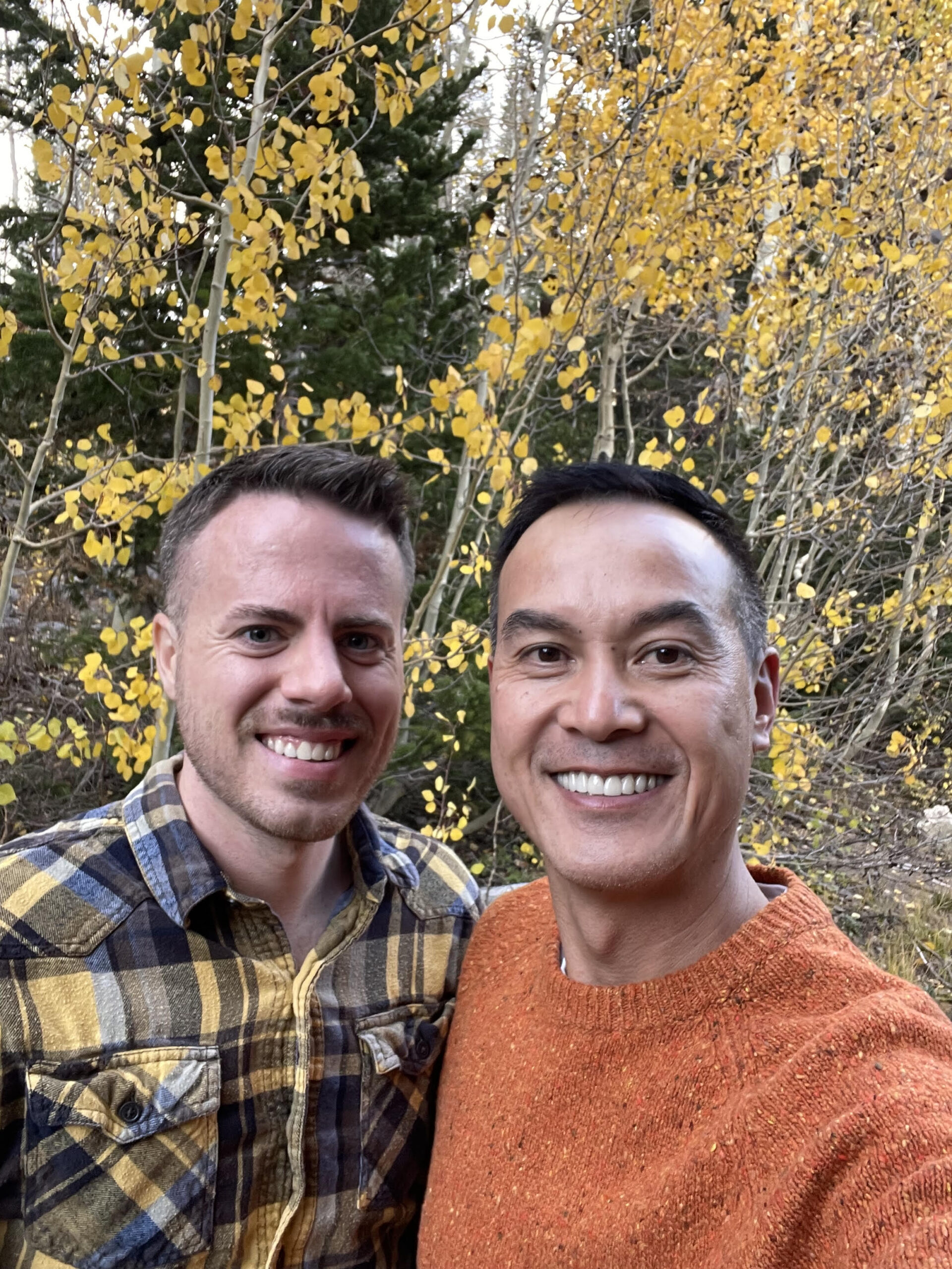 The couple visiting the canyon during the fall season and color change. A field of yellow aspens and pines in the background.